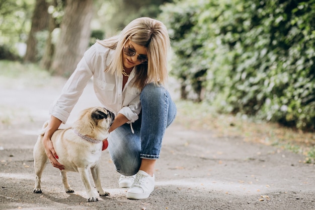 Mujer dando un paseo en el parque con su mascota perro pug Foto gratis
