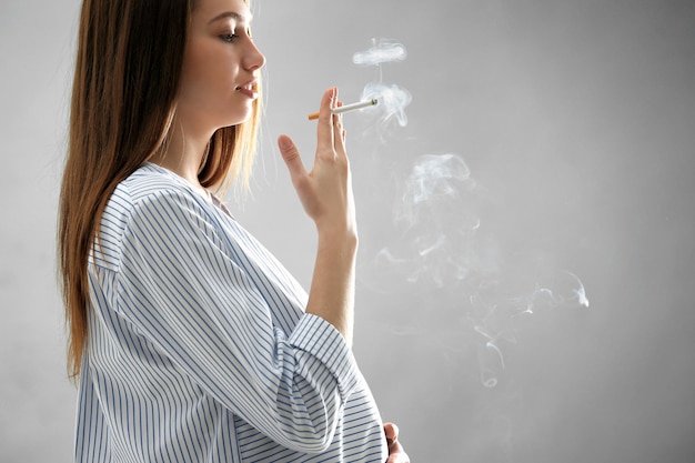Mujer Embarazada Fumando Cigarrillo Sobre Fondo Gris Foto Premium