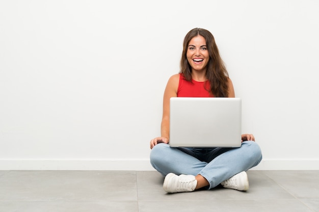 Mujer joven con una computadora portátil sentados en el suelo con expresión facial sorpresa | Foto Premium