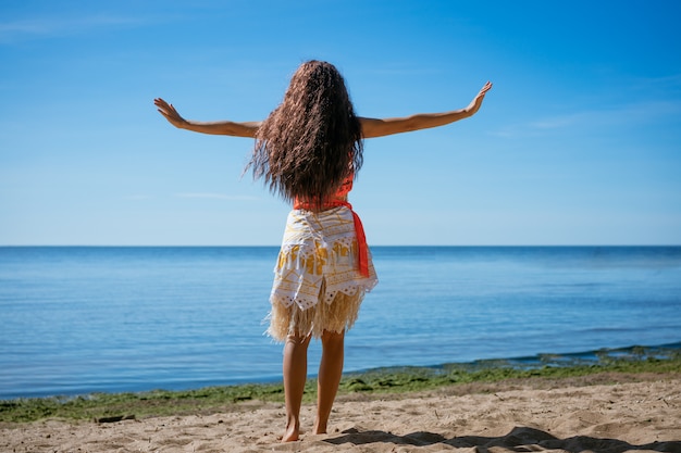 Una mujer joven se encuentra en la playa de espaldas al mar, en un día  soleado. el concepto de unas vacaciones junto al mar. | Foto Premium