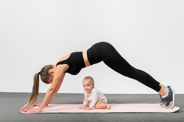 Mujer Joven En Entrenamiento De Ropa Deportiva Junto Con Su Bebe Feliz Madre Con Su Hijo Haciendo Ejercicio De Yoga Tablon Concepto De Maternidad Y Estilo De Vida Activo Foto Premium