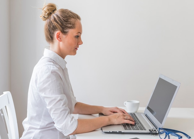 Mujer Joven Escribiendo En La Computadora Portátil Con Taza Y Anteojos En La Mesa Foto Gratis 