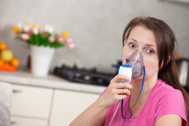 Mujer joven haciendo inhalación con un nebulizador en casa Foto Premium