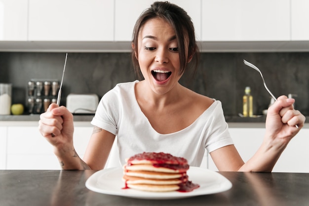 Mujer joven hambrienta sentada en la cocina en casa Foto gratis