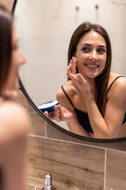 Mujer Joven Mirando Al Espejo En Casa Y Aplicando Crema En La Cara En