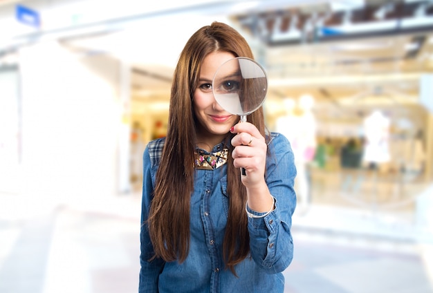 Mujer joven de moda con una lupa delante de su ojo Foto gratis