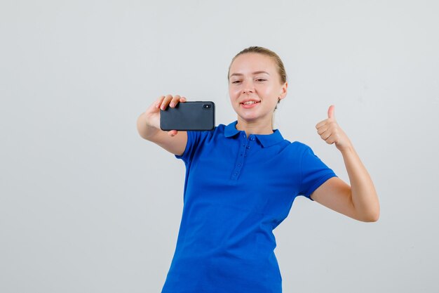 Mujer Joven Mostrando El Pulgar Hacia Arriba Mientras Toma Selfie En Camiseta Azul Foto Gratis