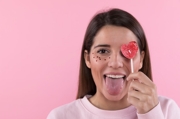 Mujer Joven Que Se Divierte Con Adornos Brilla En La Cara Y Lollipop Foto Gratis
