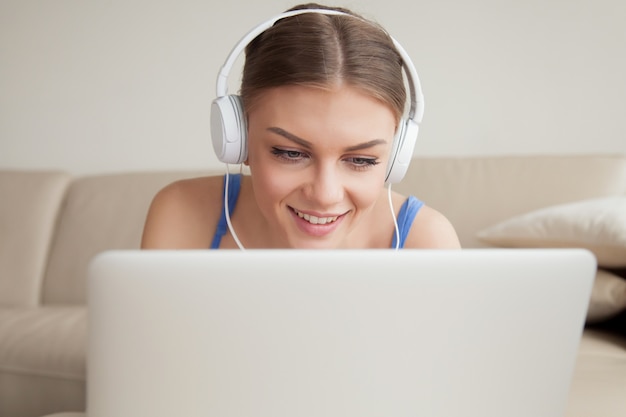 Mujer joven sonriente con auriculares usando laptop, headshot Foto gratis