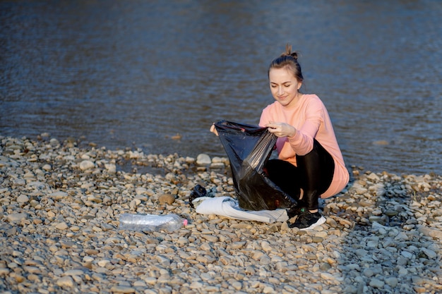 Mujer joven con su hijo recoge basura plástica en una bolsa de basura