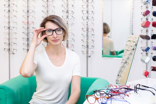 Mujer Joven En Tienda De Ptica Eligiendo Gafas Nuevas Con Ptico