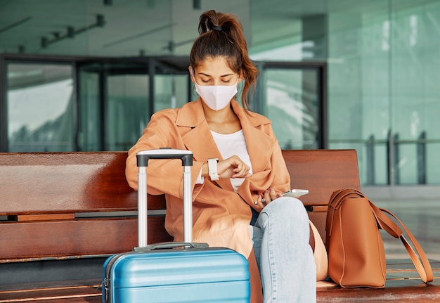 Mujer con máscara médica mirando su reloj en el aeropuerto ...