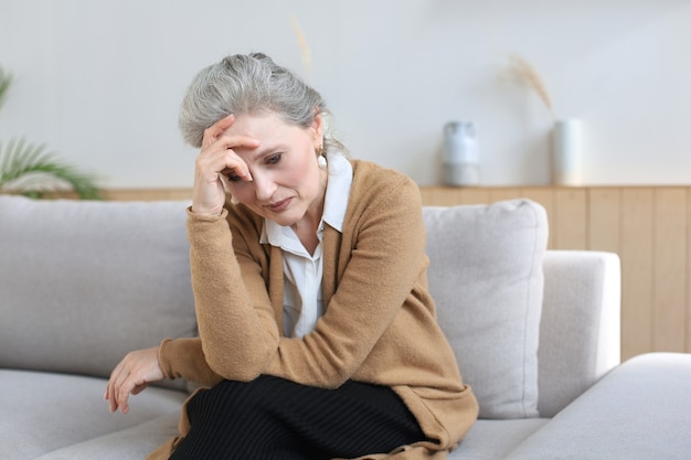 Mujer de mediana edad preocupada sentada en un sofá en la sala de estar