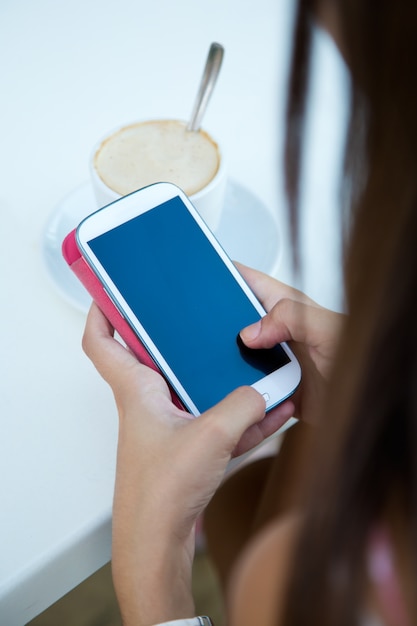 Mujer que mira el teléfono mientras que bebe el café