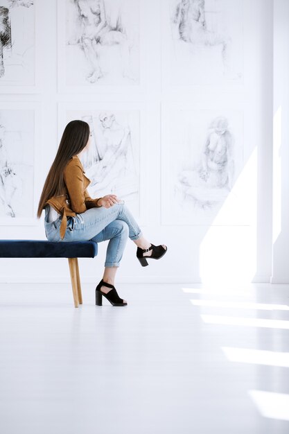 Mujer sentada en un taburete en una amplia galería con dibujos en la