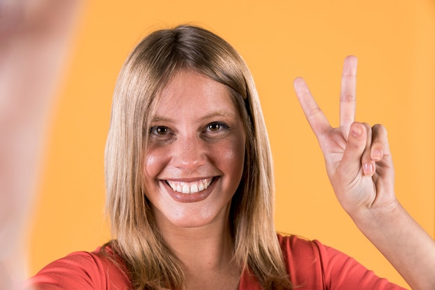 Mujer sorda sonriente que muestra signo de la victoria sobre fondo amarillo brillante Foto gratis