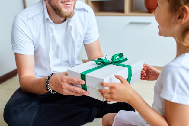 Niña le está dando a su padre guapo una caja de regalo el día del padre