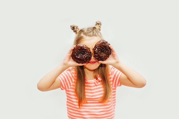 Niña linda comiendo donas dulces sobre un fondo claro Foto Premium