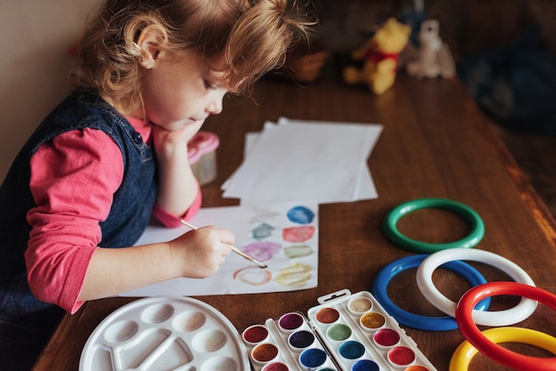Niña linda dibuja un círculo de pinturas de colores Foto gratis