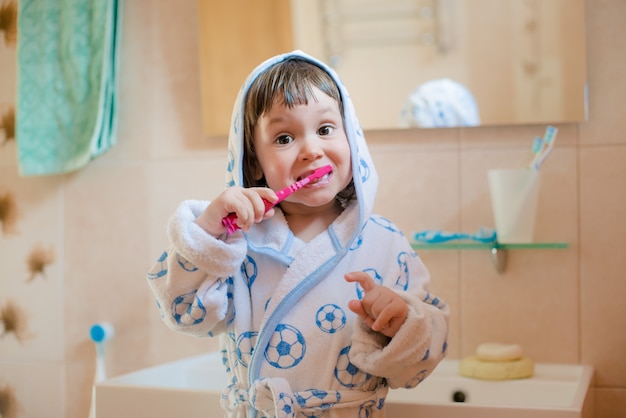 Una niña pequeña se cepilla los dientes en el baño. higiene de la cavidad oral. Foto Premium