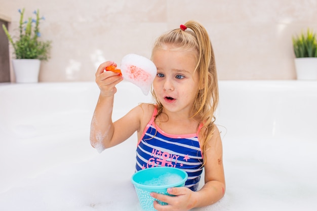 Niña rubia tomando baño de burbujas en el hermoso baño. higiene de los