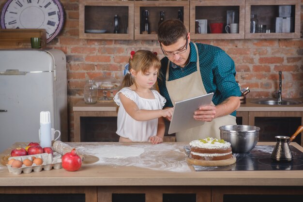 Una Niña Con Su Padre En La Cocina Con Una Tableta Digital Está Preparando La Cena Foto Premium 