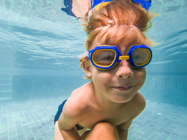 Un niño está nadando bajo el agua en una piscina sonriendo y