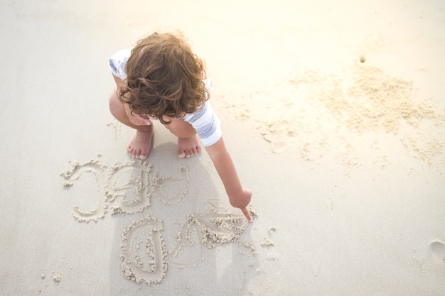 Un niño peludo está escribiendo el alfabeto inglés en la playa de arena blanca Foto Premium 