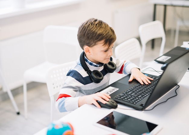 Un niño pequeño que usa la computadora portátil en el escritorio en el aula Foto gratis