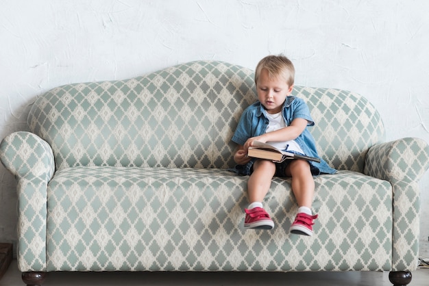 Niño Sentado En El Sofá Pasando Las Páginas Del Libro Foto Gratis 8690