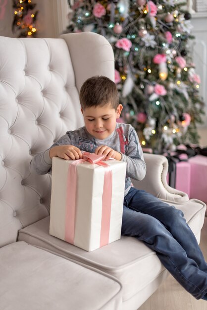 Niño sentado en el sofá y tratando de desempacar su regalo Foto Premium