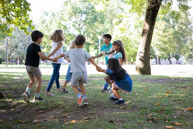 Niños felices jugando juntos al aire libre, bailando sobre el césped, disfrutando de actividades al aire libre y divirtiéndose en el parque. concepto de fiesta o amistad para niños Foto gratis