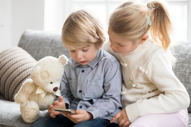 Niños y niñas con teléfono inteligente juntos sentados en el sofá Foto gratis