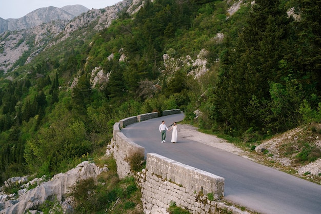 La novia y el novio están caminando por una carretera de alta montaña