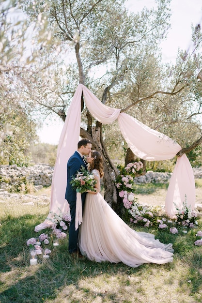 El Novio Besa A La Novia En La Frente Debajo De Un árbol En Un Parque Verde Foto Premium 