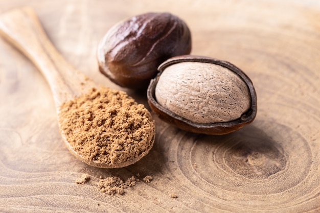 Nueces de nuez moscada entera y una cuchara con el polvo de la nuez en el primer de madera rústico de la tabla. Foto Premium