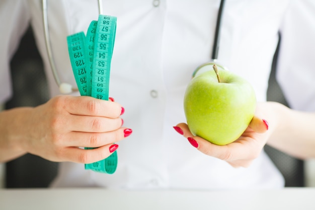 Nutricionista femenina y sosteniendo una manzana y una cinta métrica. Foto Premium