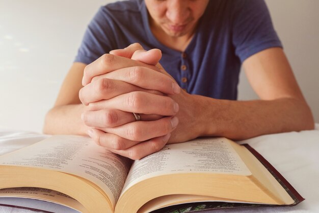 Orando las manos de un hombre sobre la biblia abierta en la cama blanca Foto Premium
