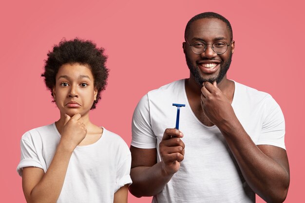 Un Padre Alegre Sostiene La Maquina De Afeitar Se Toca La Barba Espesa Y Le Dice A Un Adolescente Como Afeitarse Correctamente Foto Gratis