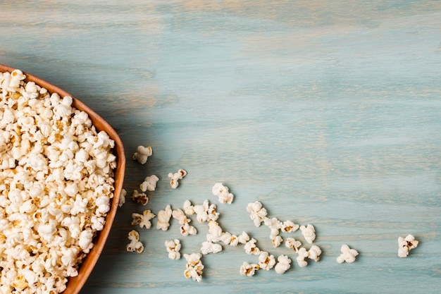 Palomitas de maíz se derramó del tazón en el escritorio azul Foto gratis