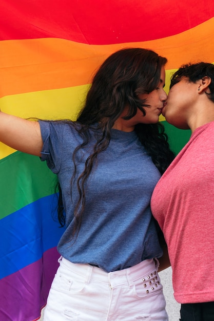 Un Par De Chicas Besándose Con Una Bandera Del Orgullo Gay Al Aire Libre Foto Premium