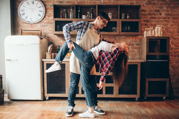 Pareja De Amor Juguetón Posa En La Cocina Hombre En Delantal Y Mujer Joven Están Bailando 7584