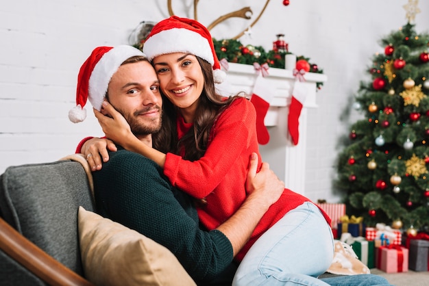 Pareja Feliz En Sombreros De Navidad Abrazando En Sofa Foto Gratis