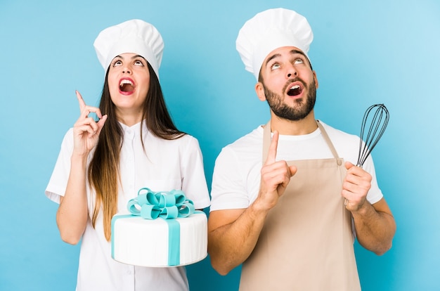 Pareja joven cocinando un pastel juntos aislado apuntando al revés con