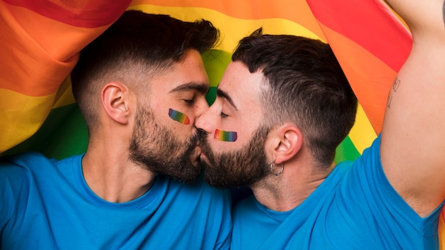 Pareja De Jóvenes Homosexuales De Hombres Besándose En Bandera Lgbt Foto Gratis