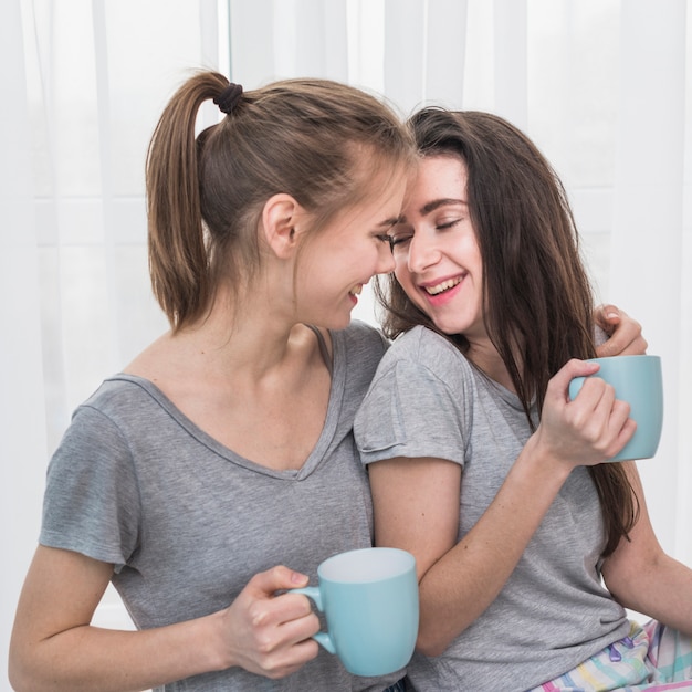 Pareja De Lesbianas Jovenes Romanticas Felices En Camiseta Gris Sosteniendo Una Taza De Cafe Azul En La Mano Foto Gratis