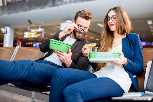 Pareja De Negocios Elegante Comiendo Con Loncheras Sentado En La Sala De Espera En El Aeropuerto