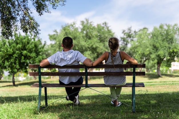 Pareja sentada en un banco de madera debajo de un árbol mirando hacia adelante Foto Premium