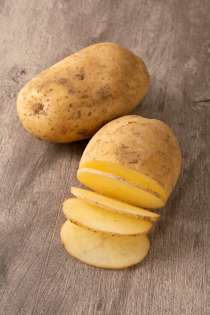 Patata cruda y patata cortada sobre fondo de madera | Foto Premium