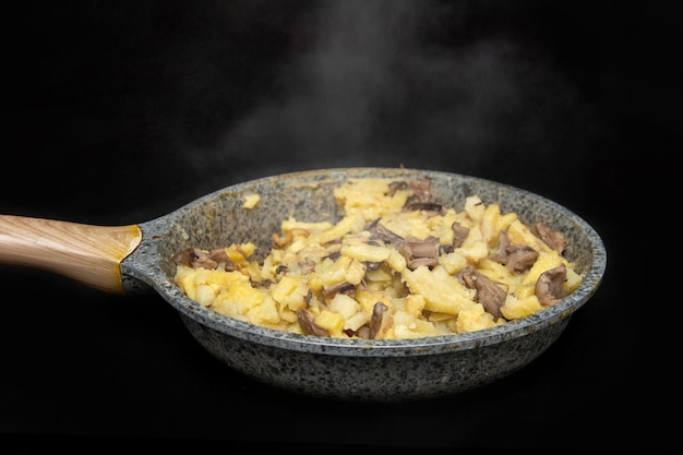 Patatas fritas con champiñones en una sartén manchada de gris sobre una  mesa negra, recién cocida, vapor de freír, fondo oscuro | Foto Premium